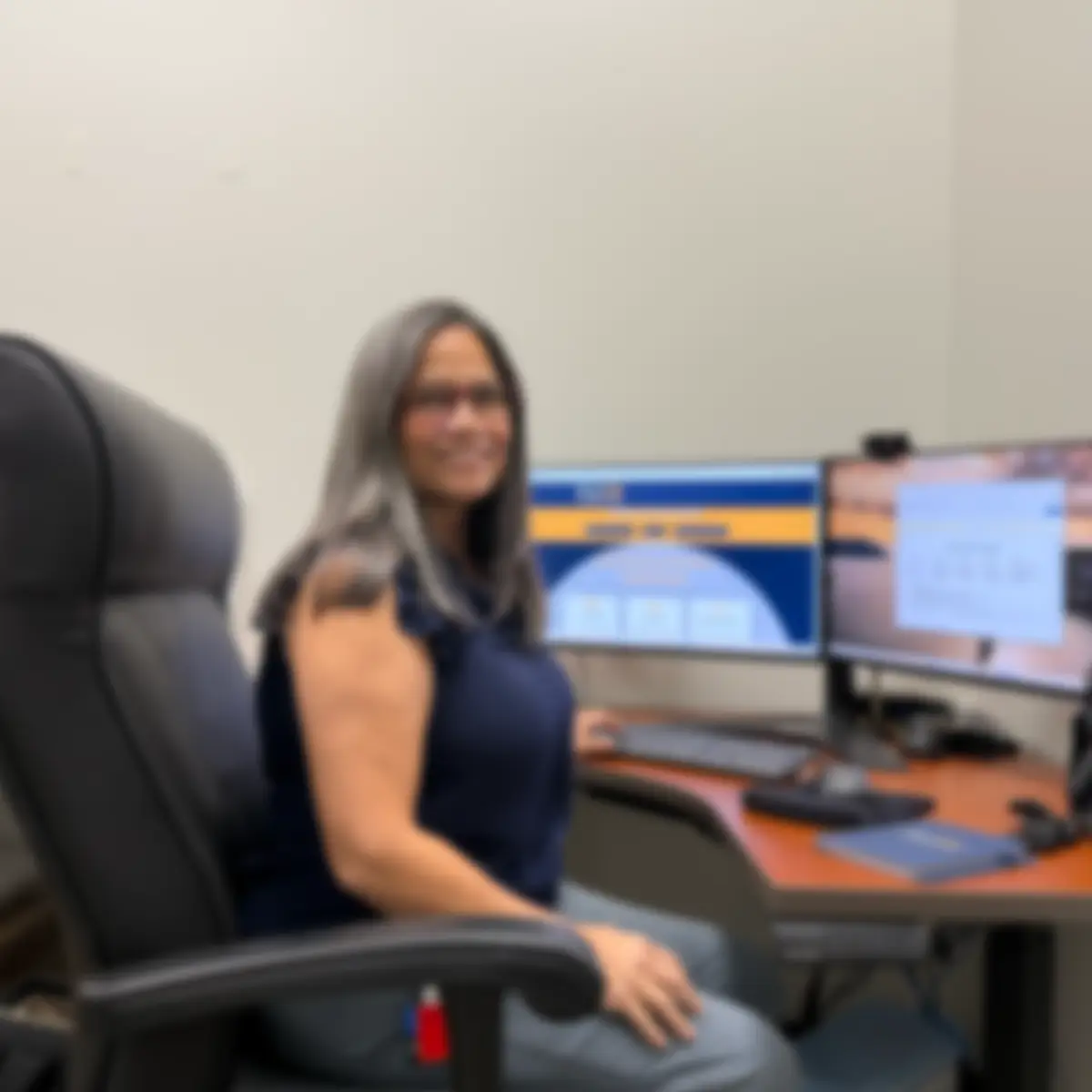 Woman seated at an office desk with two computer monitors in front of her (blurry image). ,